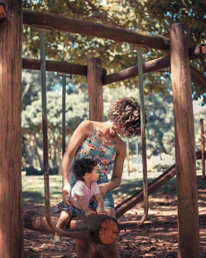 Une mère aide sa fille à monter sur une balançoire dans un parc